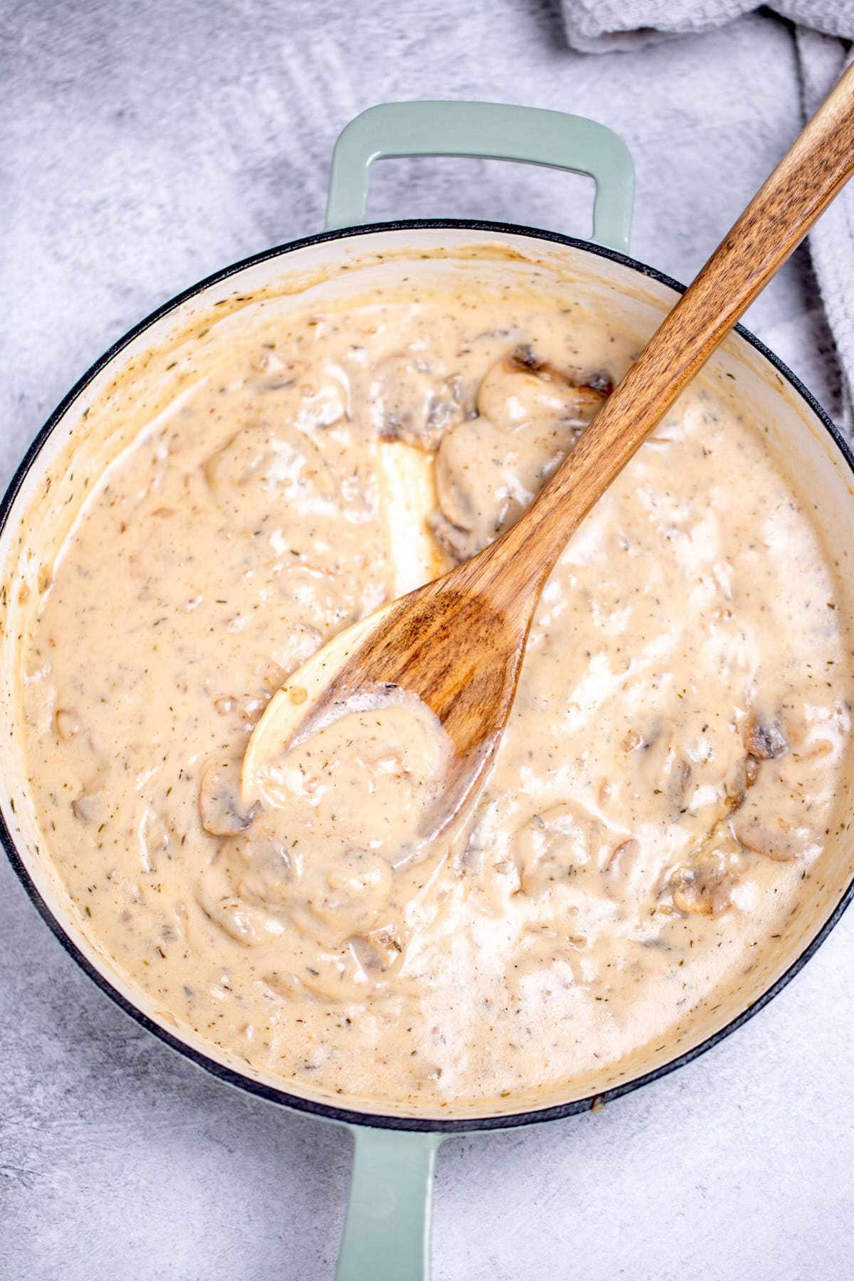 A skillet with mushroom sauce and a wooden spoon resting in it.