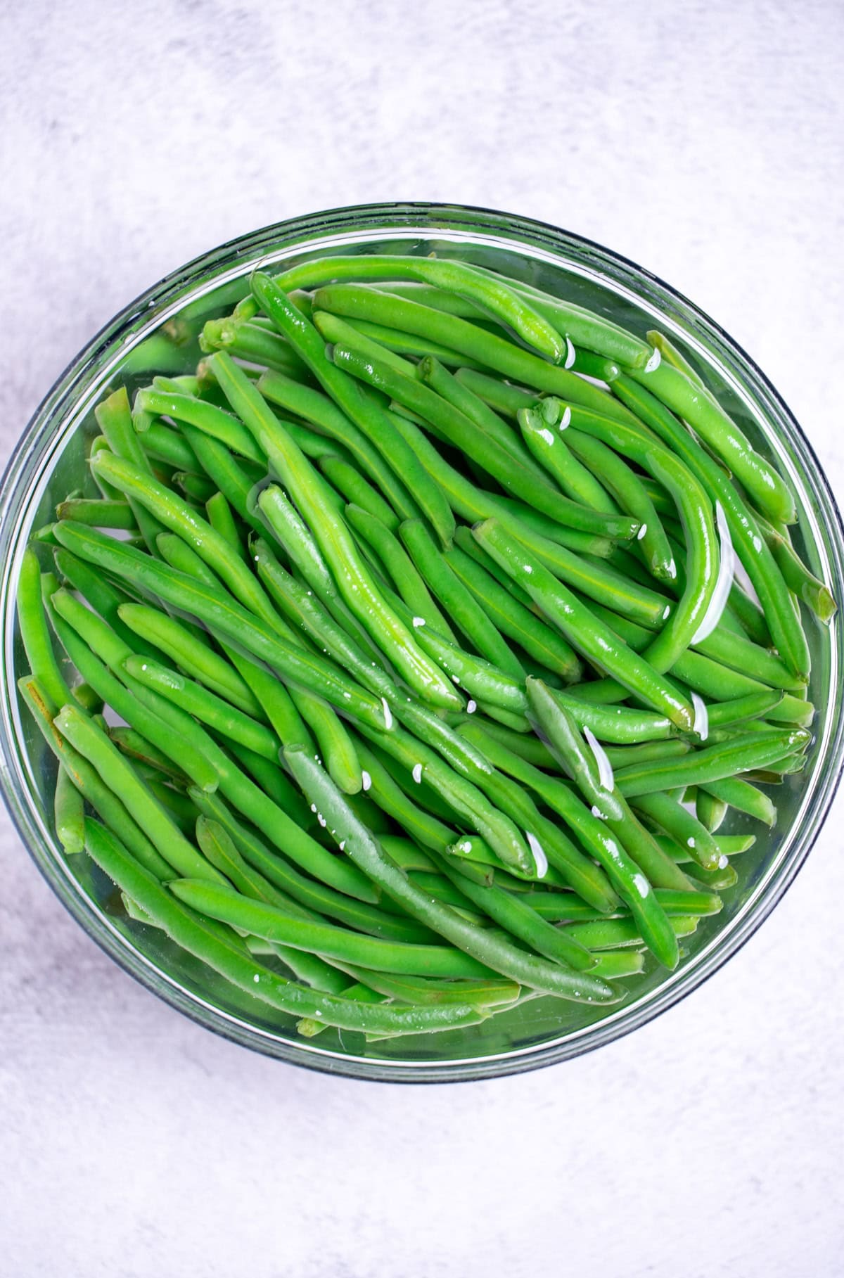 A bowl of blanched green beans in ice water on a table.