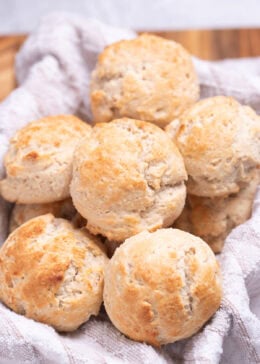 A basket with a tea towel full of gluten free drop biscuits resting on top of each other.