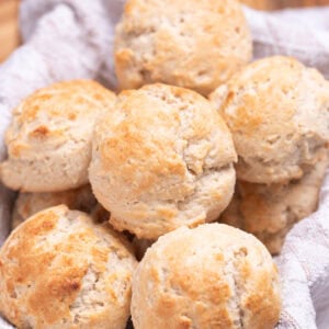 A basket with a tea towel full of gluten free drop biscuits resting on top of each other.