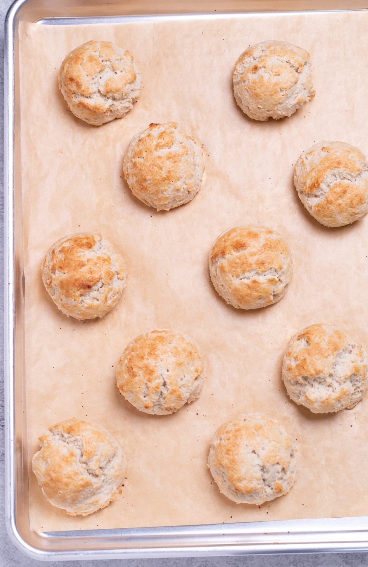 Gluten free buttermilk drop biscuits spread out on a baking sheet lined with parchment paper.