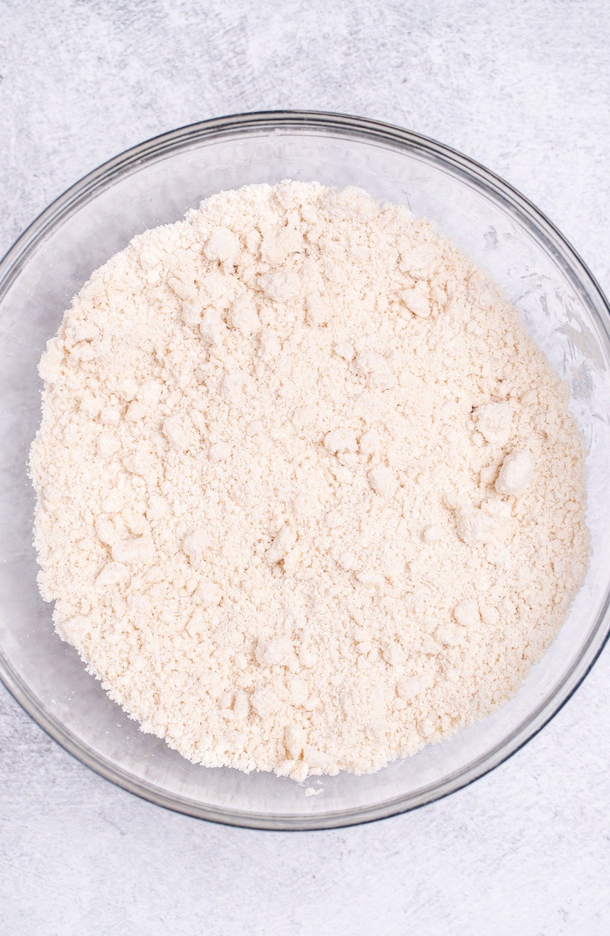 A mixing bowl on a table, with flour that's had butter cut into it with small pea-sized pieces of butter in it.