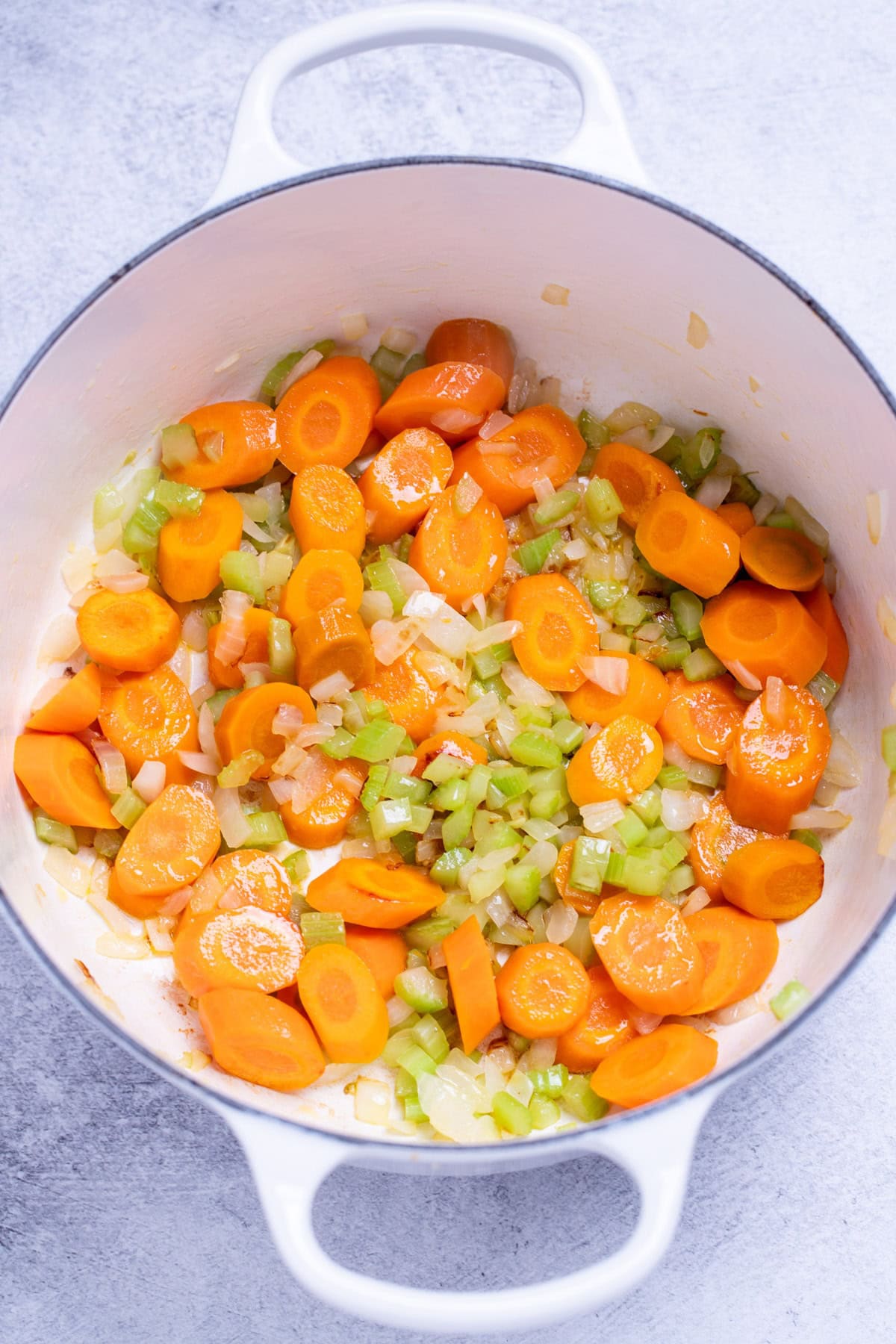 A dutch oven with chopped carrots, onion, and celery being sautéed in olive oil.