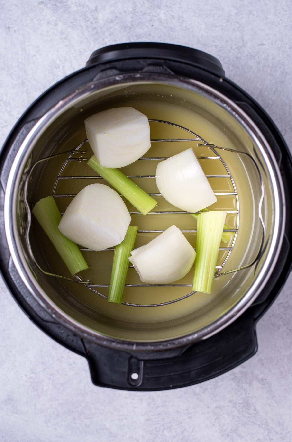 An instant pot with a trivet, broth, onion and celery.