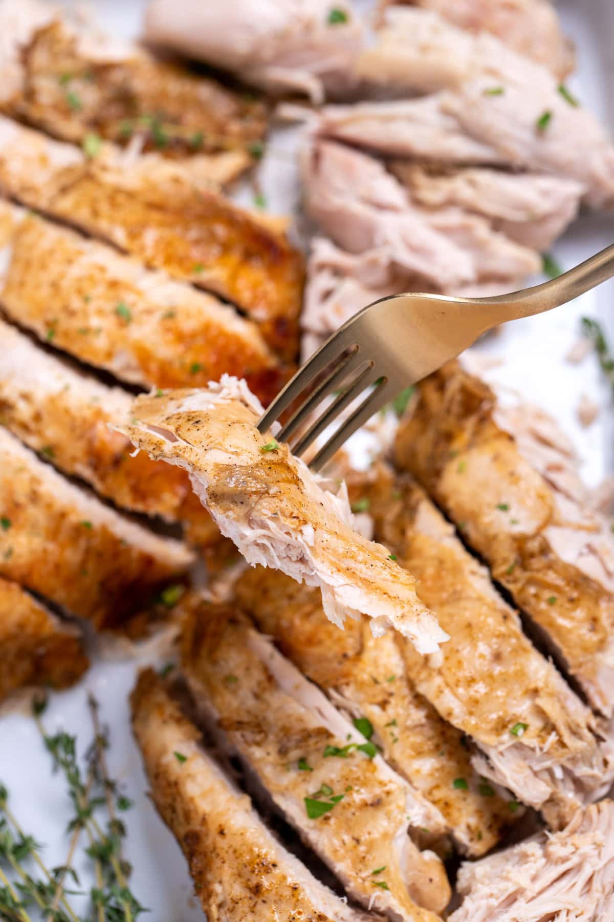 A baking dish of turkey breast slices, with a fork lifting one up.