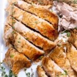 A baking dish with carved turkey breast and fresh thyme.