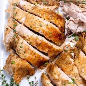 A baking dish with carved turkey breast and fresh thyme.