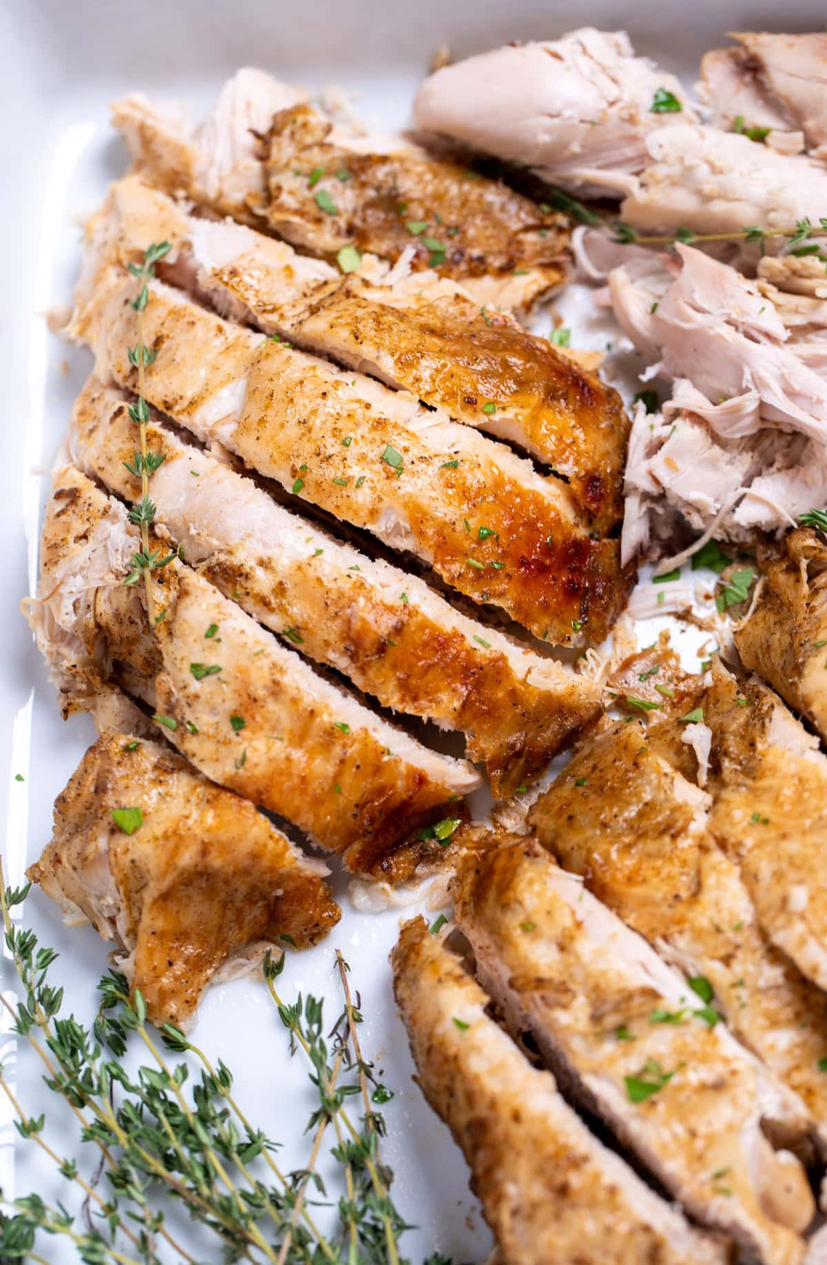 A baking dish with carved turkey breast and fresh thyme.