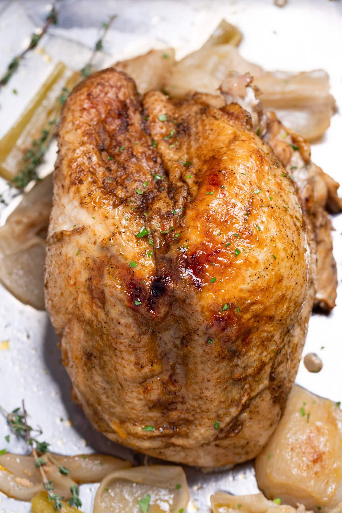 A bone-in turkey breast in a roasting pan with onion, celery, and thyme, after being broiled.