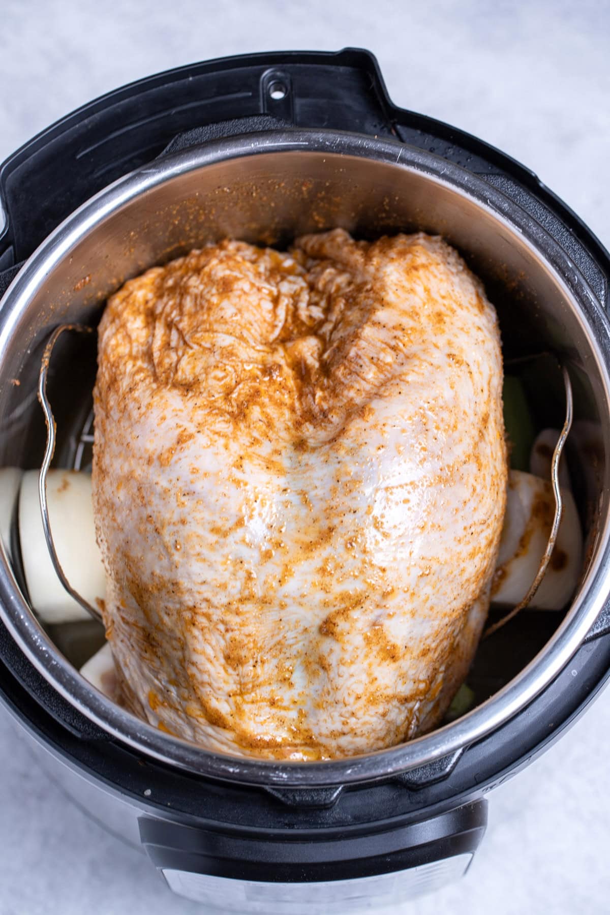 A bone-in turkey breast rubbed with seasoning and olive oil in an instant pot on top of onion, before being cooked.