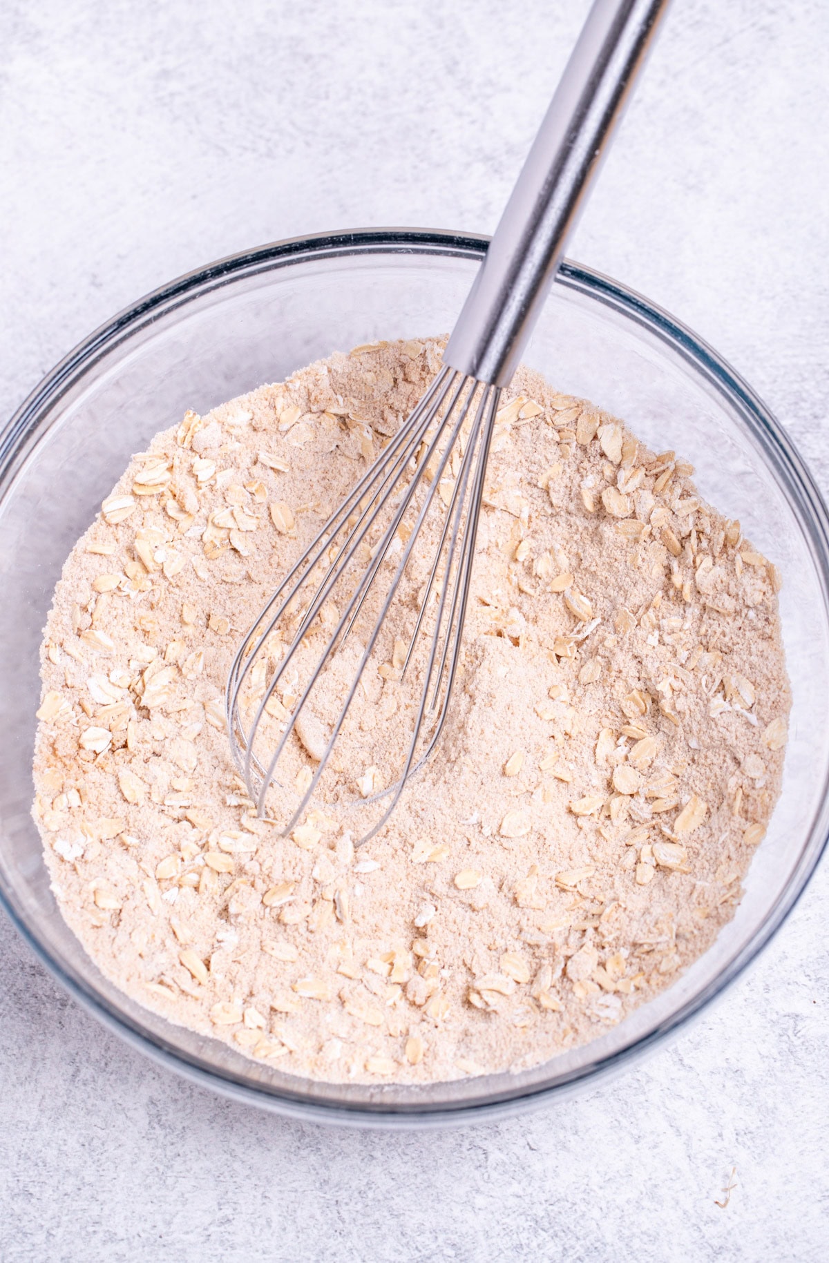 A mixing bowl with the dry ingredients for the oat topping whisked together, with a whisk resting in the bowl.