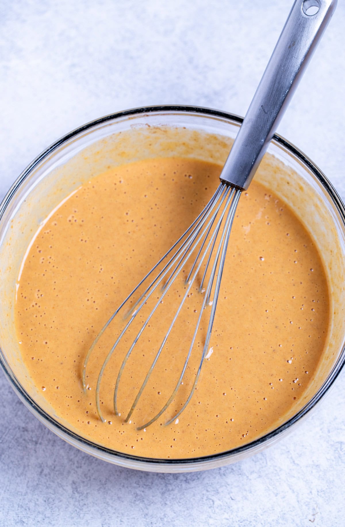 A mixing bowl with the pumpkin pie filling after being whisked together, with a whisk resting in the bowl.