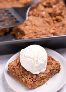 A plate with a serving of pumpkin crisp topped with ice cream in front of the baking dish of crisp.