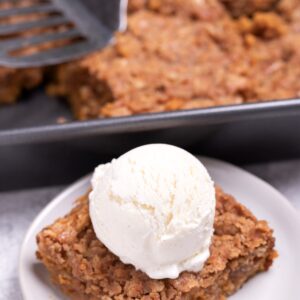 A plate with a serving of pumpkin crisp topped with ice cream in front of the baking dish of crisp.