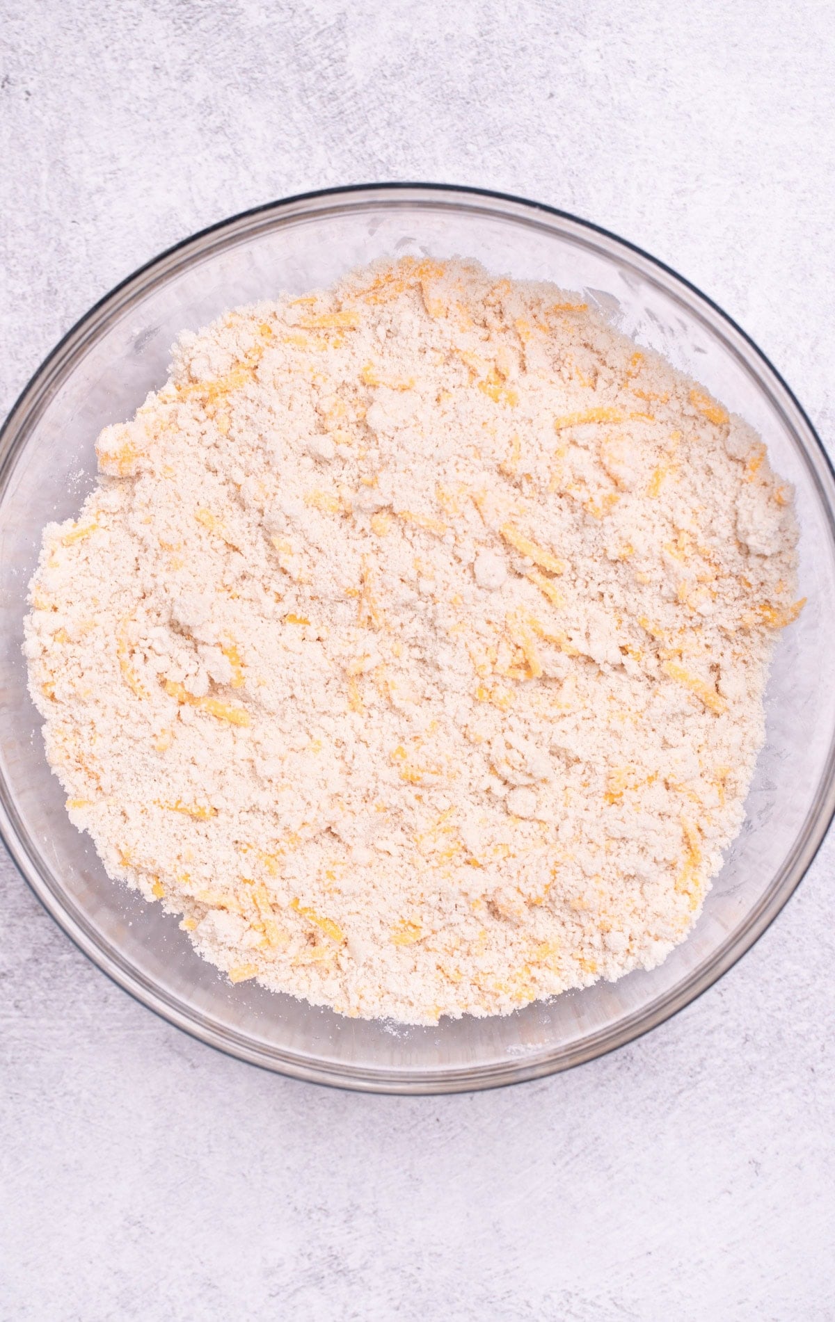 A mixing bowl on a table with flour, butter, and shredded cheddar mixed together.