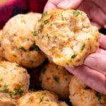 A hand tearing open a gluten free cheddar bay biscuit, over a basket of other biscuits.
