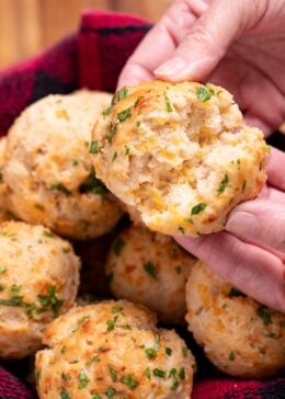 A hand tearing open a gluten free cheddar bay biscuit, over a basket of other biscuits.