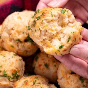 A hand tearing open a gluten free cheddar bay biscuit, over a basket of other biscuits.