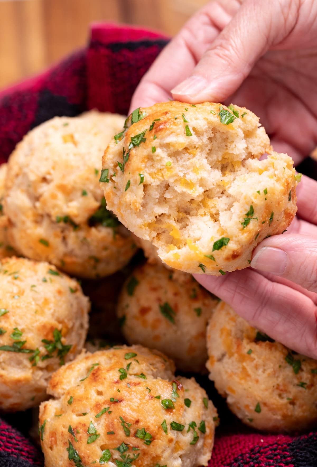 A hand tearing open a gluten free cheddar bay biscuit, over a basket of other biscuits.