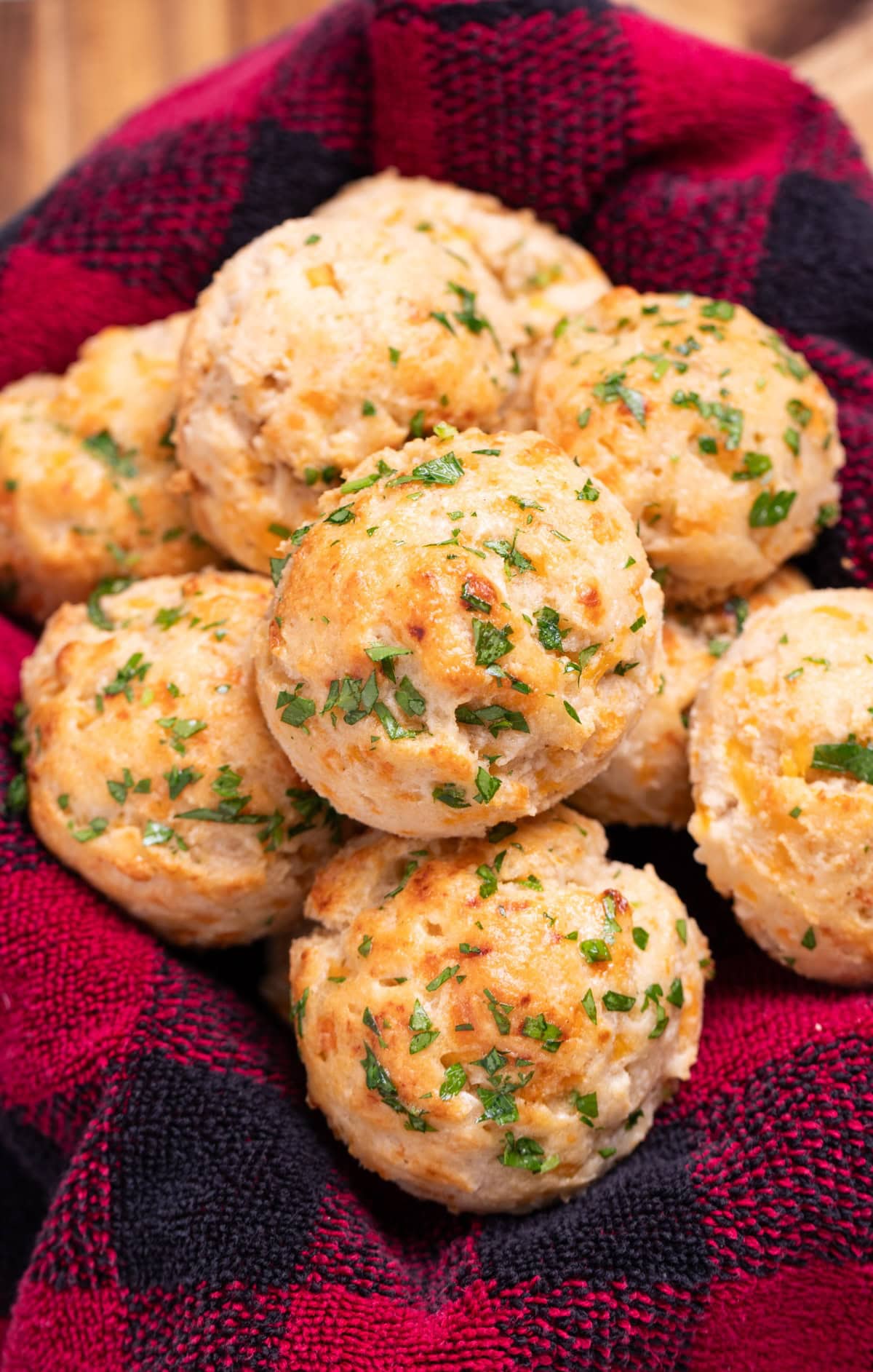 A tea towel in a basket, with homemade Red Lobster cheddar bay biscuits piled in it, topped with fresh parsley and butter.