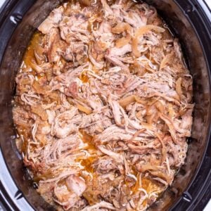 A slow cooker full of shredded apple cider pulled pork.