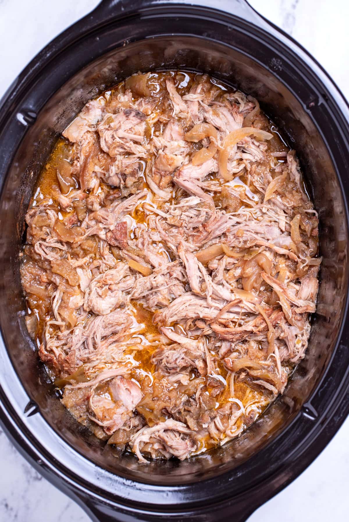 A slow cooker full of shredded apple cider pulled pork.