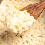 Creamed corn in a slow cooker, with a wooden spoon lifting some up.