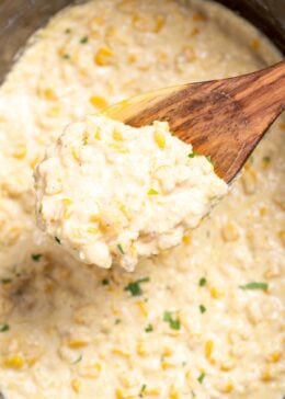 Creamed corn in a slow cooker, with a wooden spoon lifting some up.