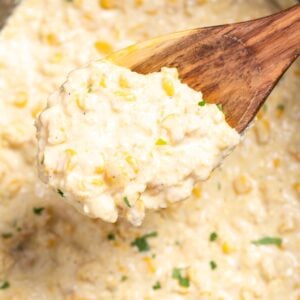 Creamed corn in a slow cooker, with a wooden spoon lifting some up.