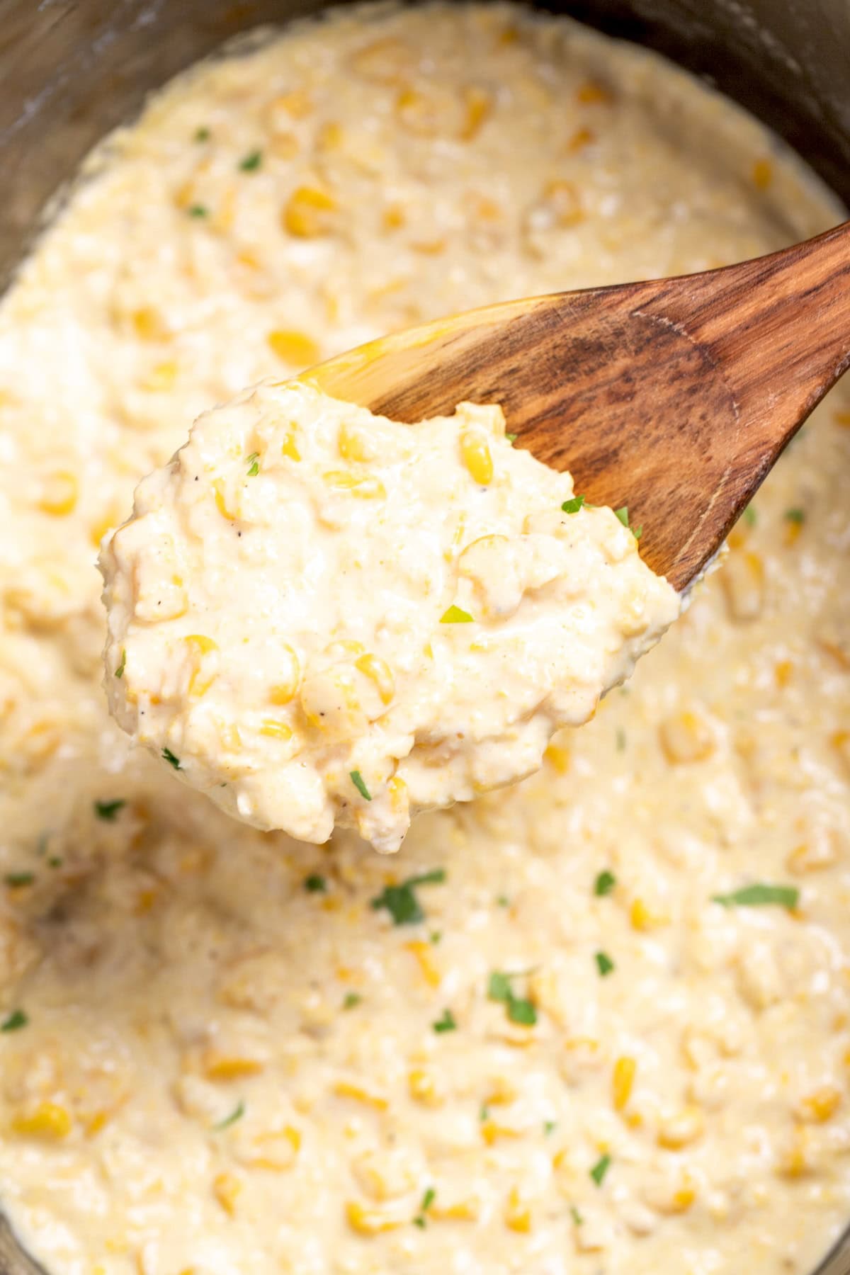 Creamed corn in a slow cooker, with a wooden spoon lifting some up.