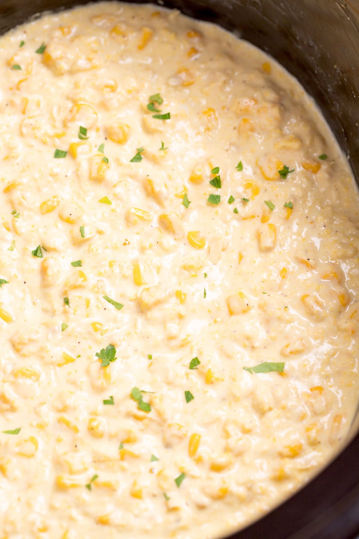 A slow cooker with creamed corn topped with fresh parsley.