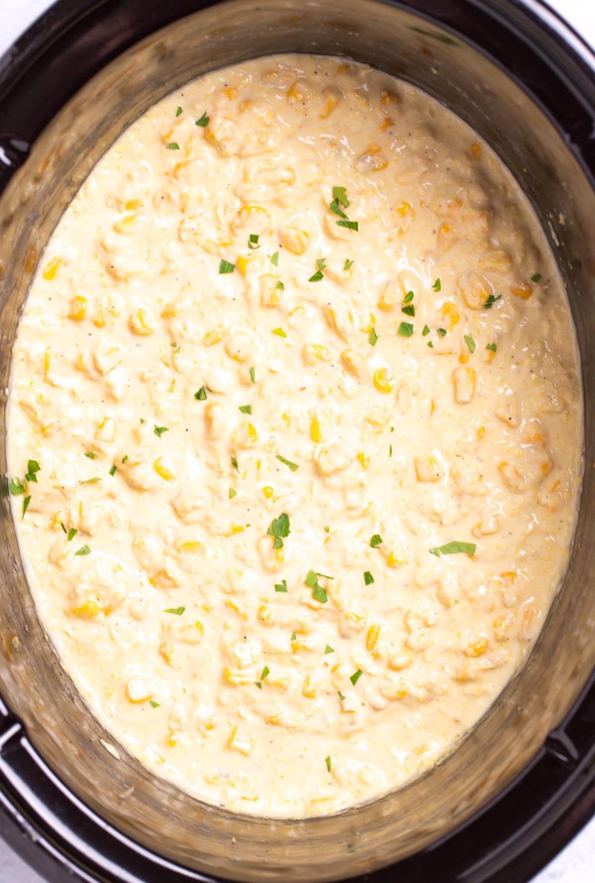 A slow cooker full of creamed corn topped with fresh parsley pieces.