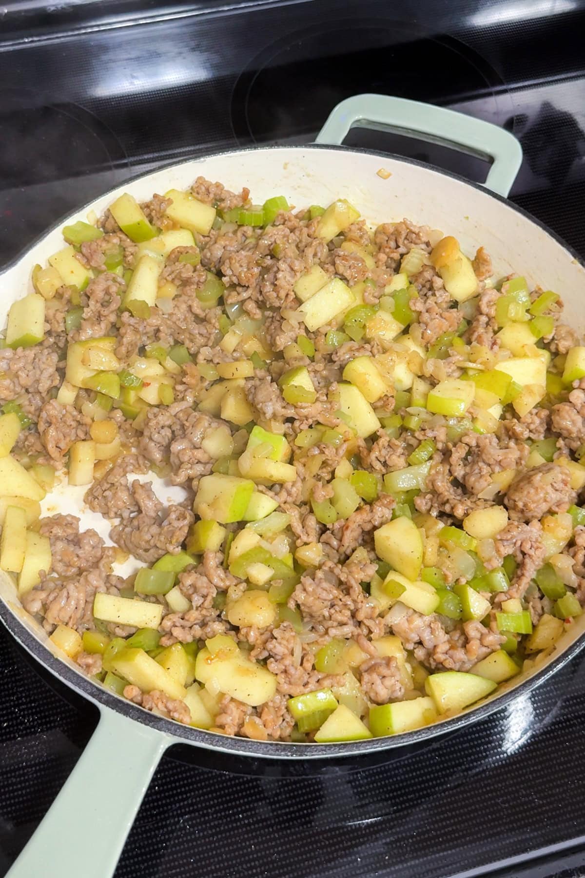 A cast iron pan with sausage, apples, onion, and parsnips cooking together.