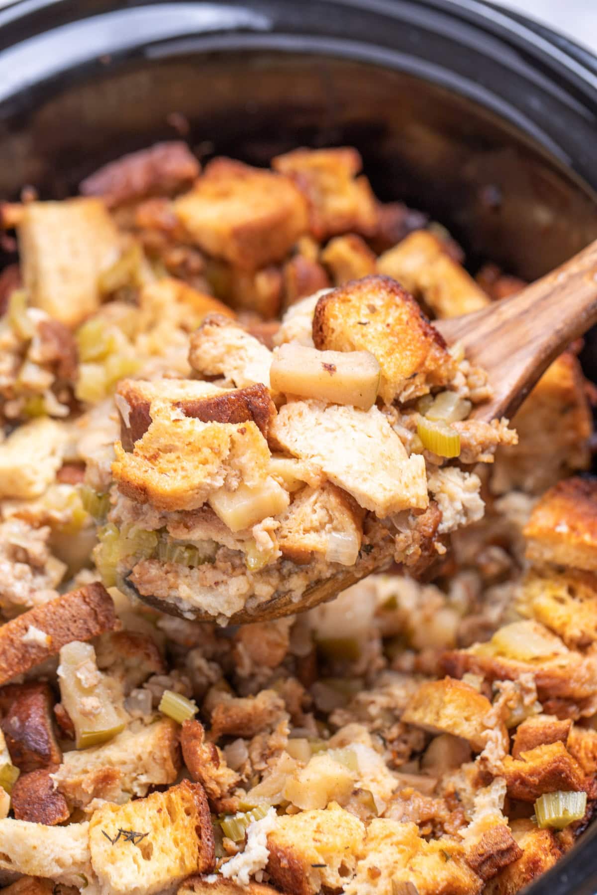 A slow cooker with a wooden spoon lifting gluten free sausage stuffing up.
